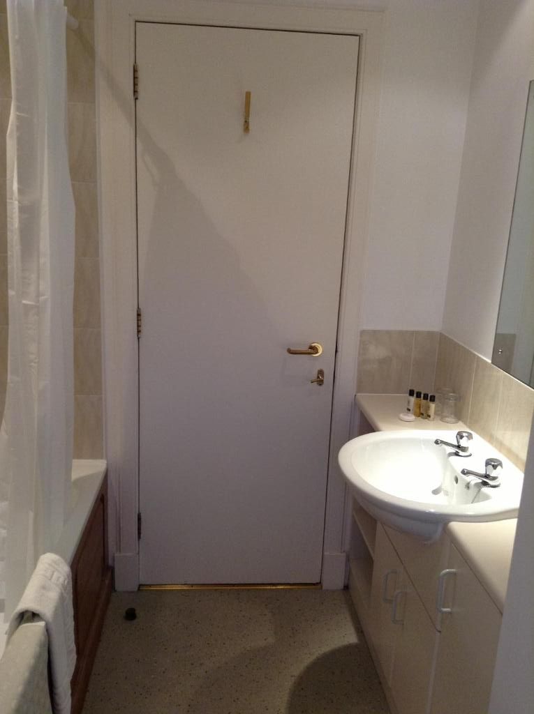 Un baño con puerta blanca, lavamanos y espejo.