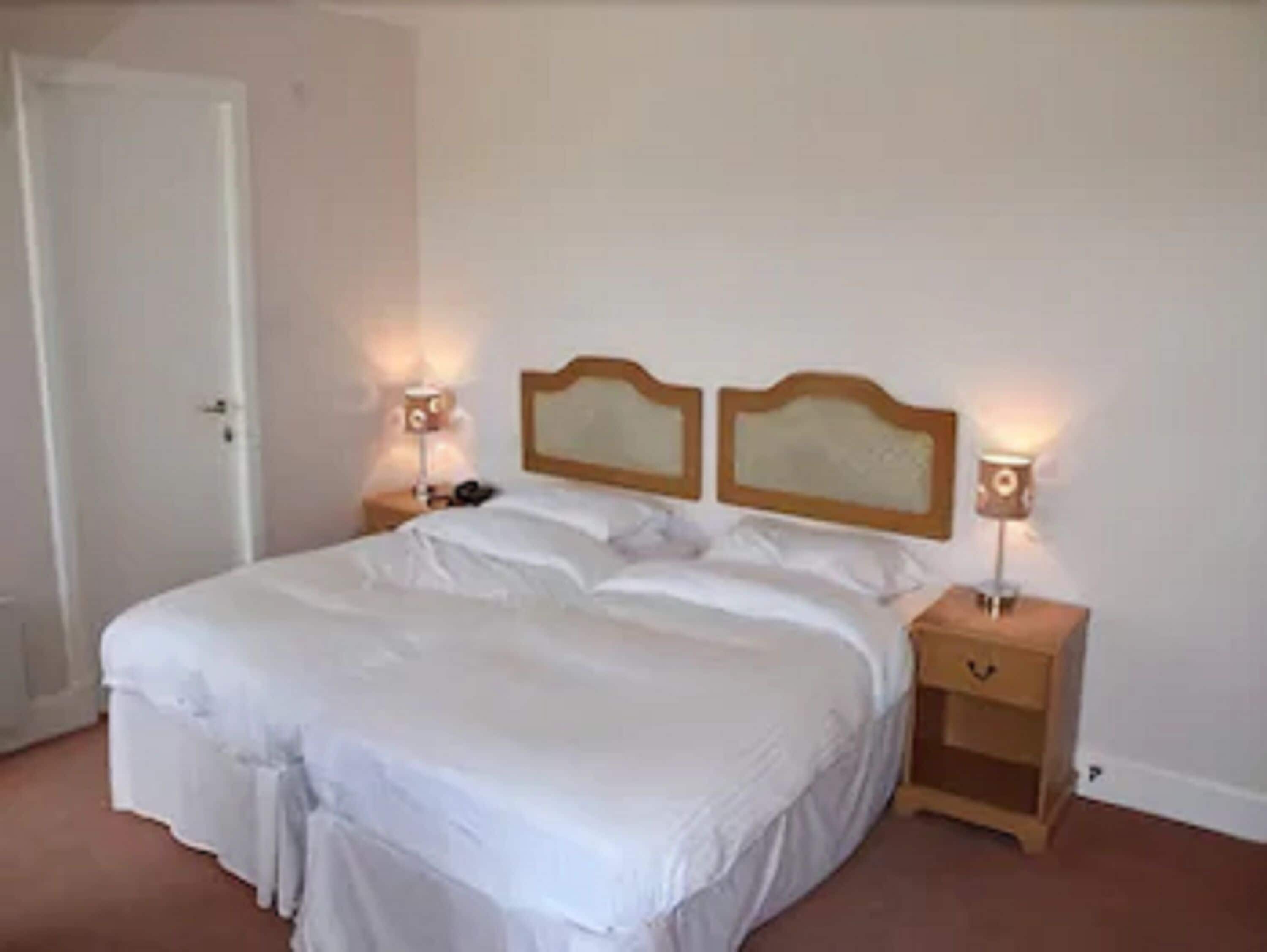 A neatly made bed with white linens, two bedside tables with lamps, and a wooden headboard.