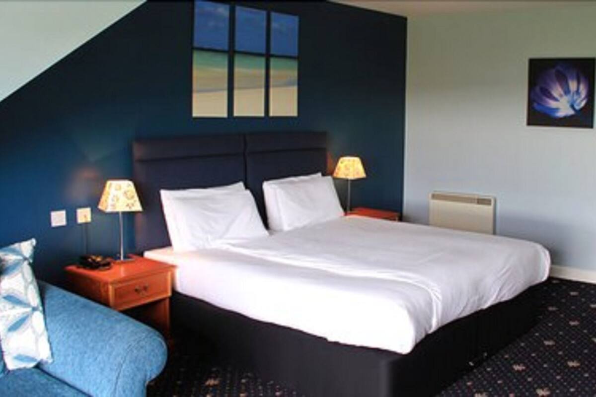 A bedroom with a bed, two bedside tables, a nightstand, a lamp, and a wall-mounted radiator.