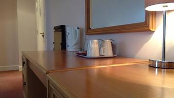 Una zona de cocina con cafetera, dos tazas blancas y una lámpara sobre una encimera de madera.