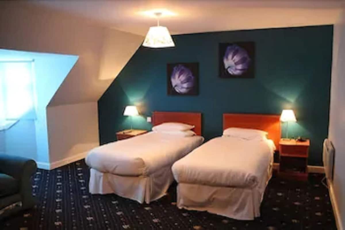 A hotel room with two single beds, a small desk, a chair, and a window.