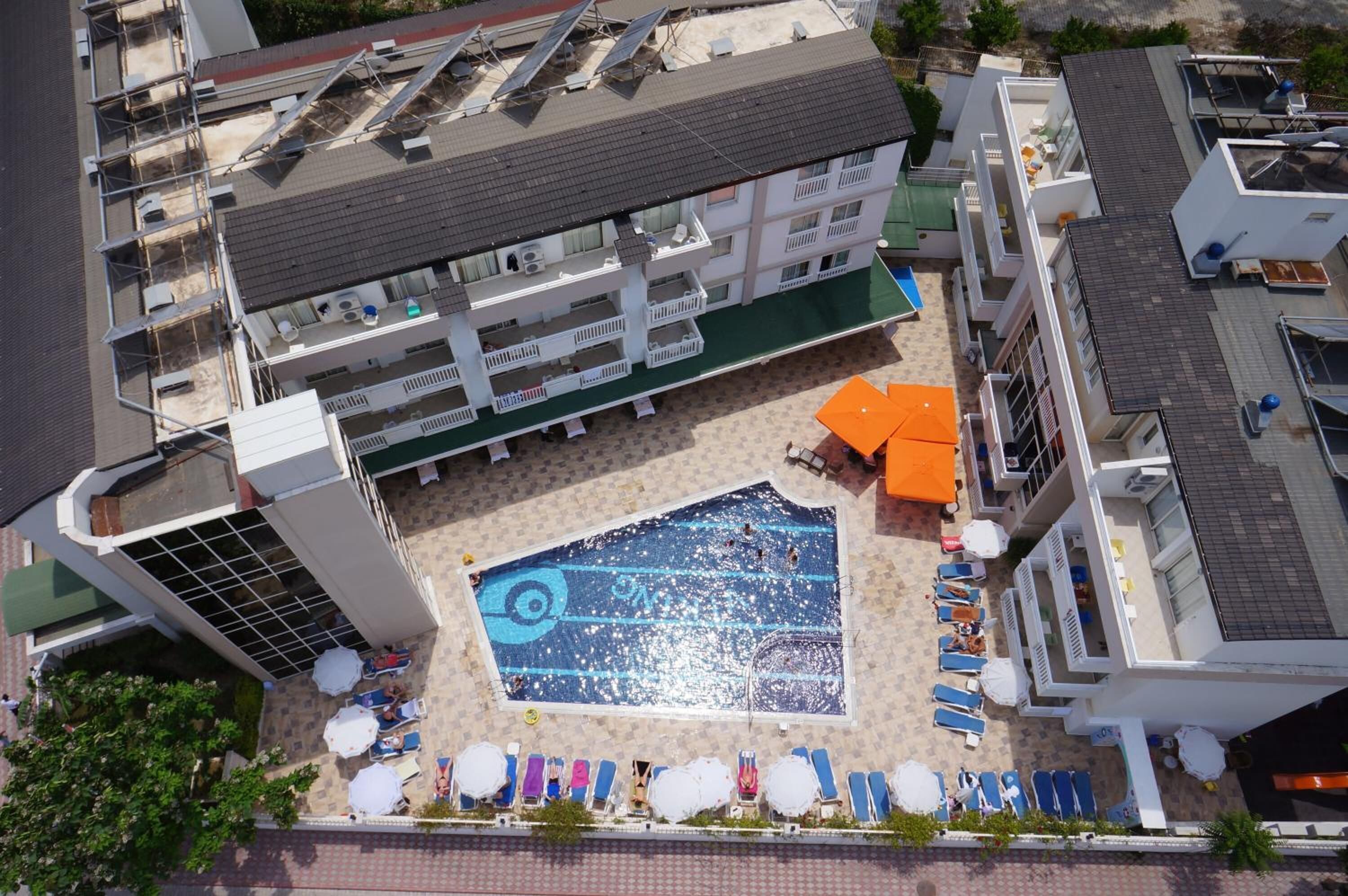Luchtbeeld van een hotel met een dakterraszwembad, omringd door ligbedden en parasols, een overdekt terras met zitplaatsen en een gebouw met meerdere balkons.