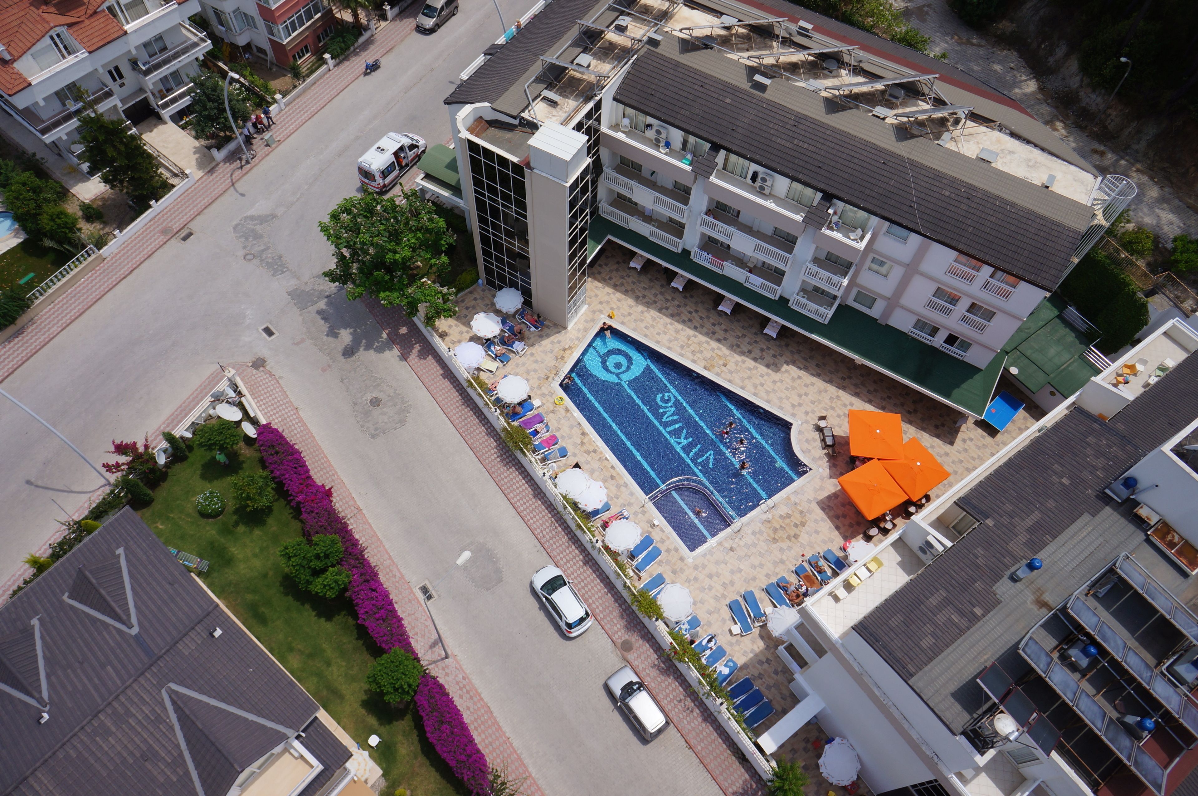 An aerial view of a hotel with a swimming pool, multiple balconies, and a parking area.