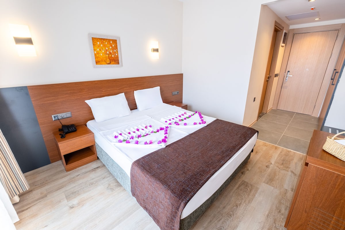 Ein Hotelzimmer mit einem hölzernen Kopfteil, weißer Bettwäsche, einem Nachttisch mit Telefon und einer Nachttischlampe.