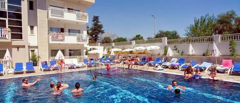 Una piscina con gente disfrutando del agua, rodeada de sillones de descanso y sombrillas.