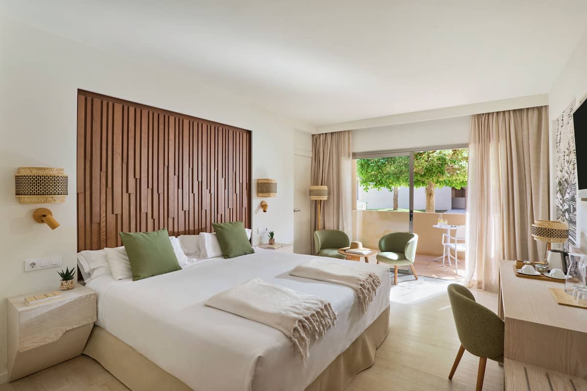 A modern hotel room with a large bed, a desk, and a view of the outdoors.