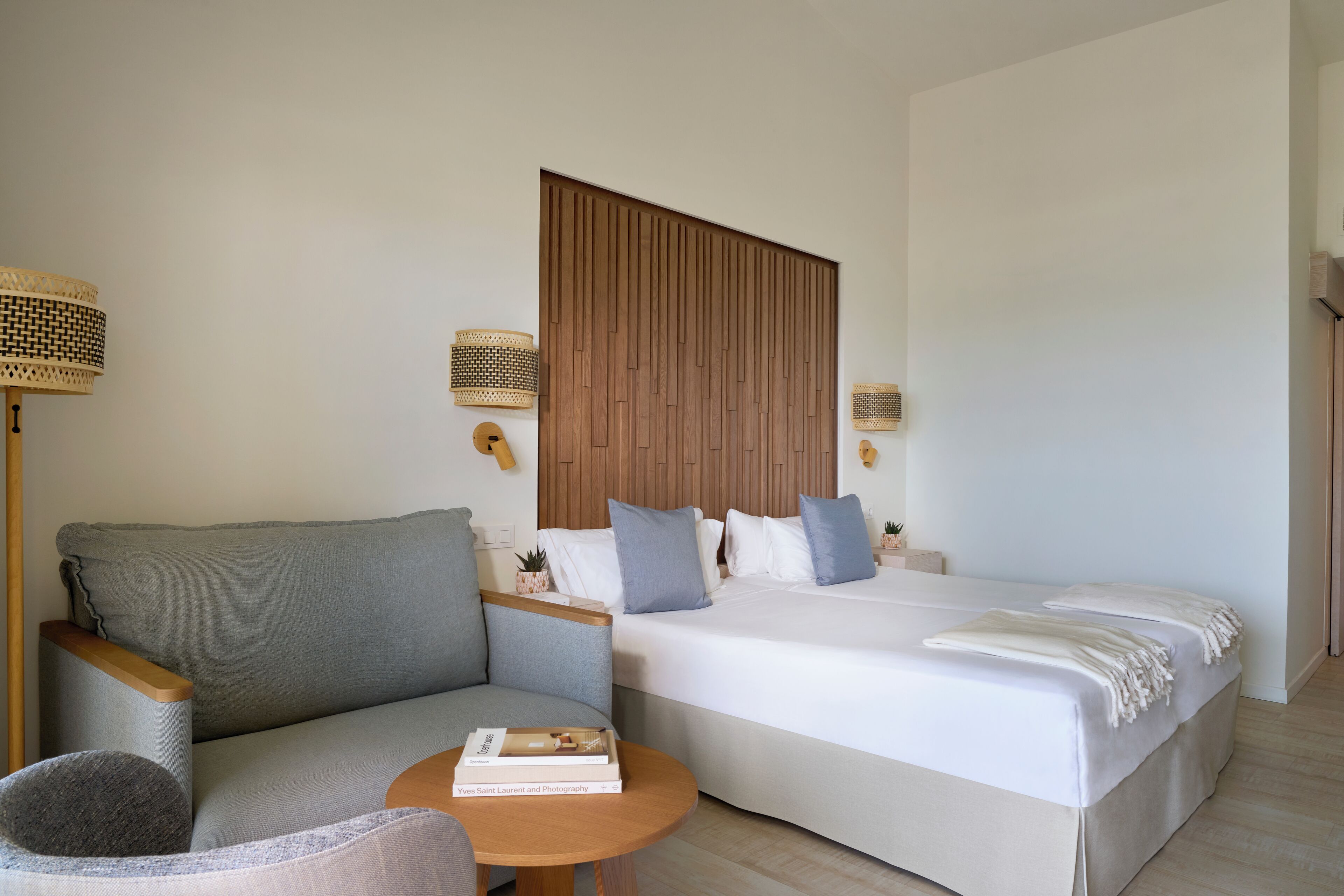 Una camera d'albergo moderna con un divano, un letto, un tavolino e due lampade a parete.
