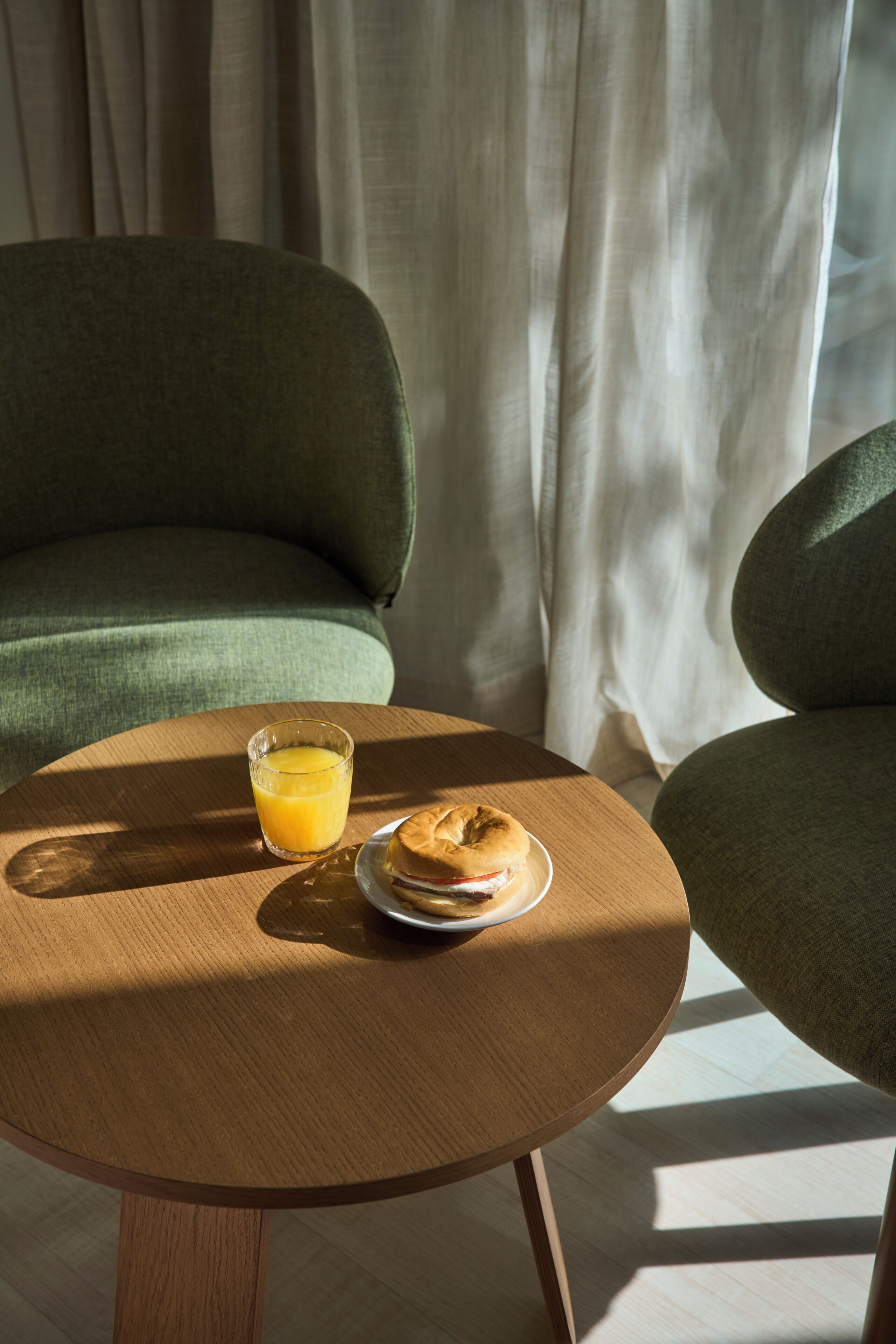 Una mesa de madera redonda con un vaso de jugo de naranja y un plato con un bagel y queso crema.
