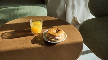 Una mesa de madera redonda con un vaso de jugo de naranja y un plato con un bagel y queso crema.