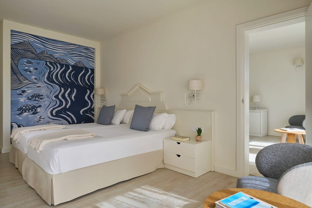 A modern hotel room with a large bed, bedside tables, a small desk, and a seating area.