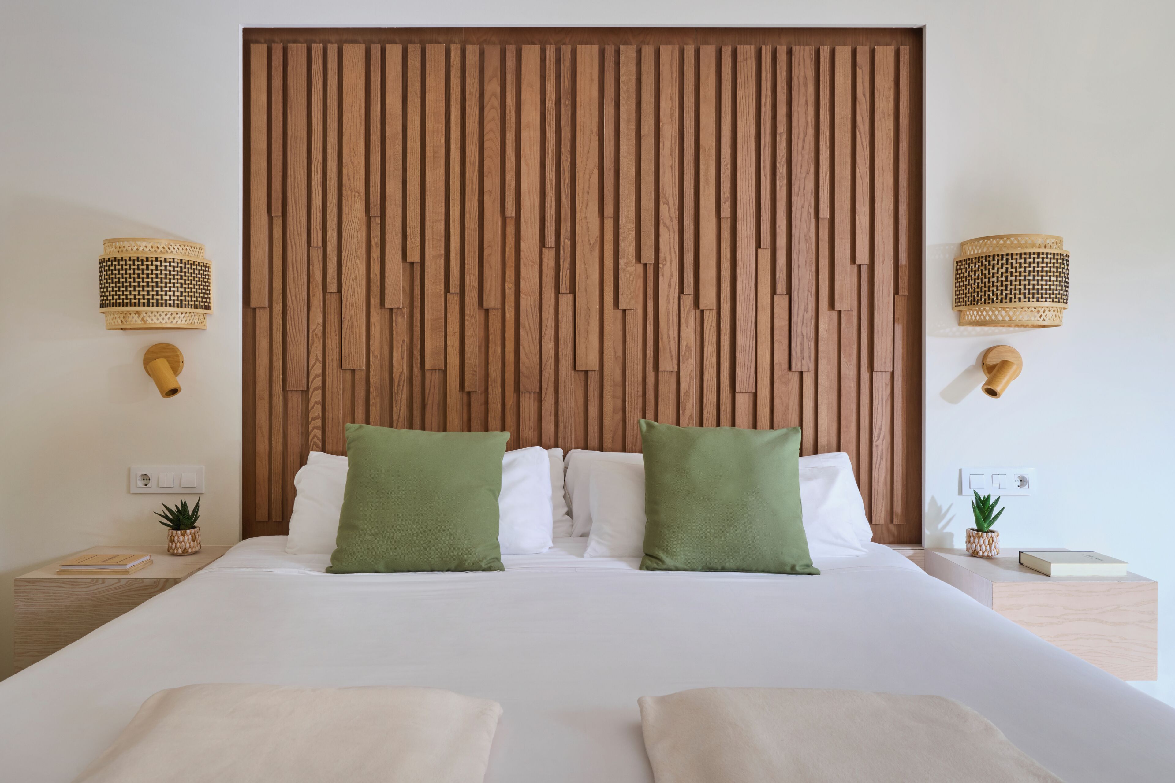 A neatly made bed with two green pillows, a wooden headboard, and two wall-mounted lamps.