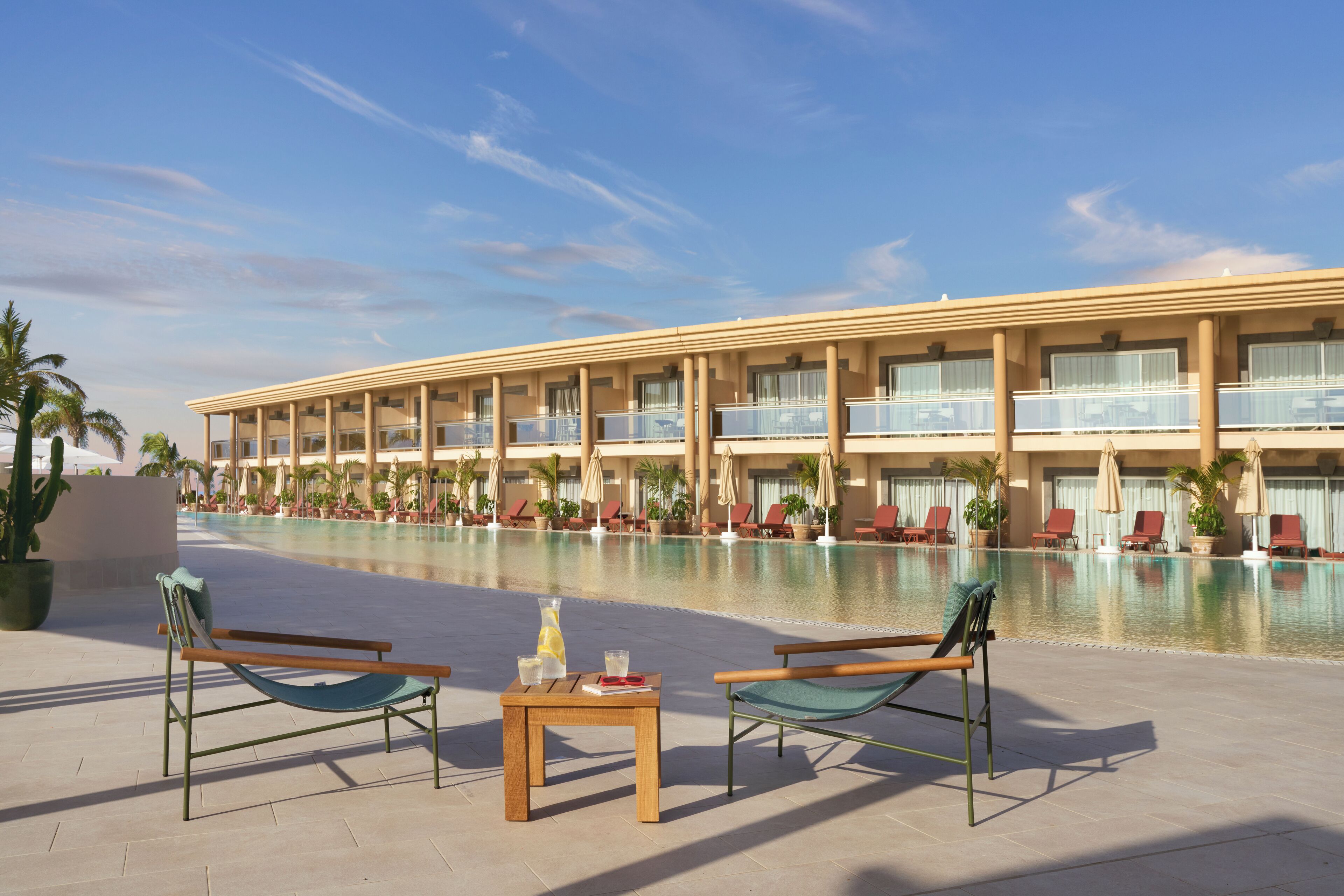 A hotel with a pool area, lounge chairs, and a table with drinks.