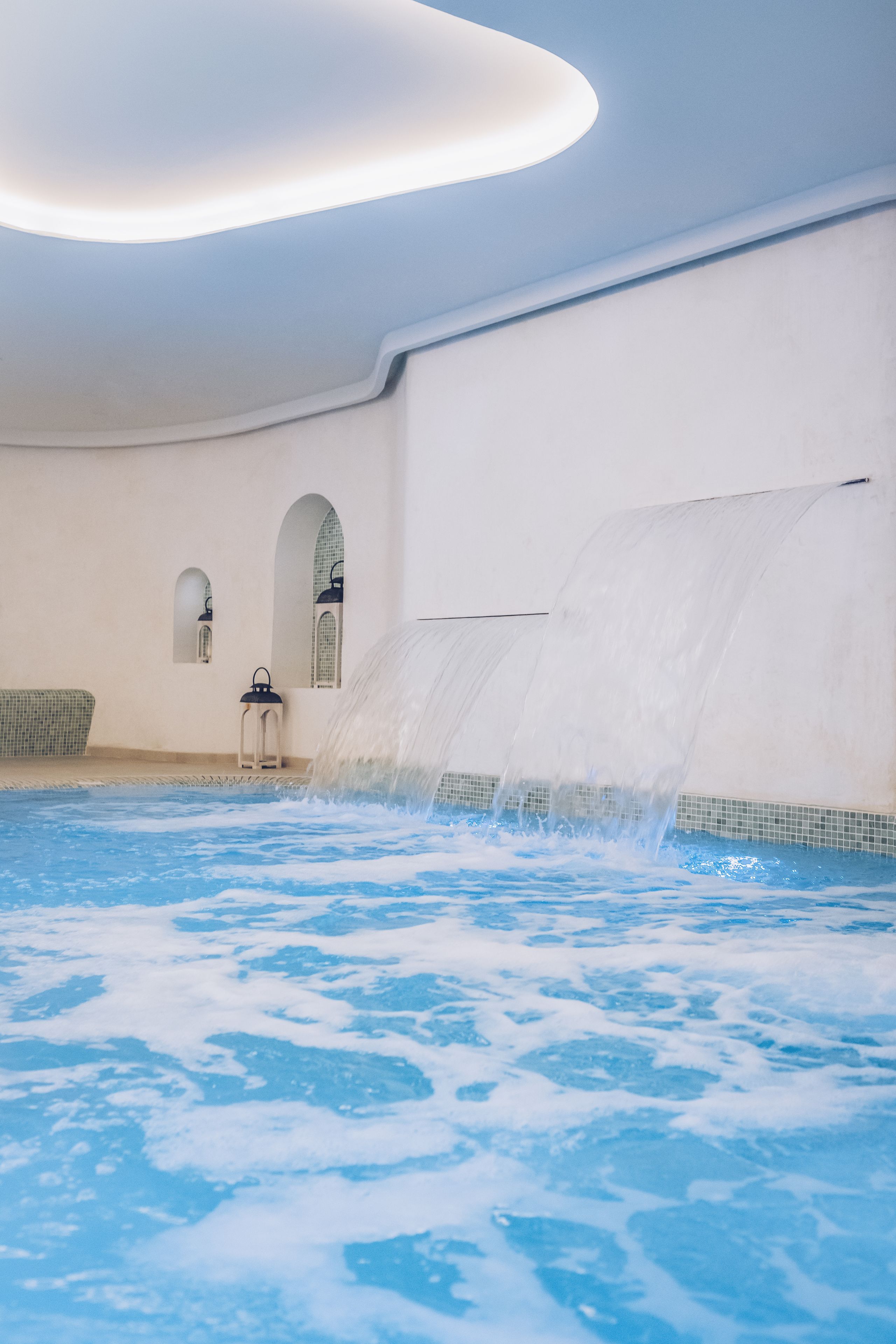 A spa area with a hot tub, a wall-mounted waterfall, and a small seating area.