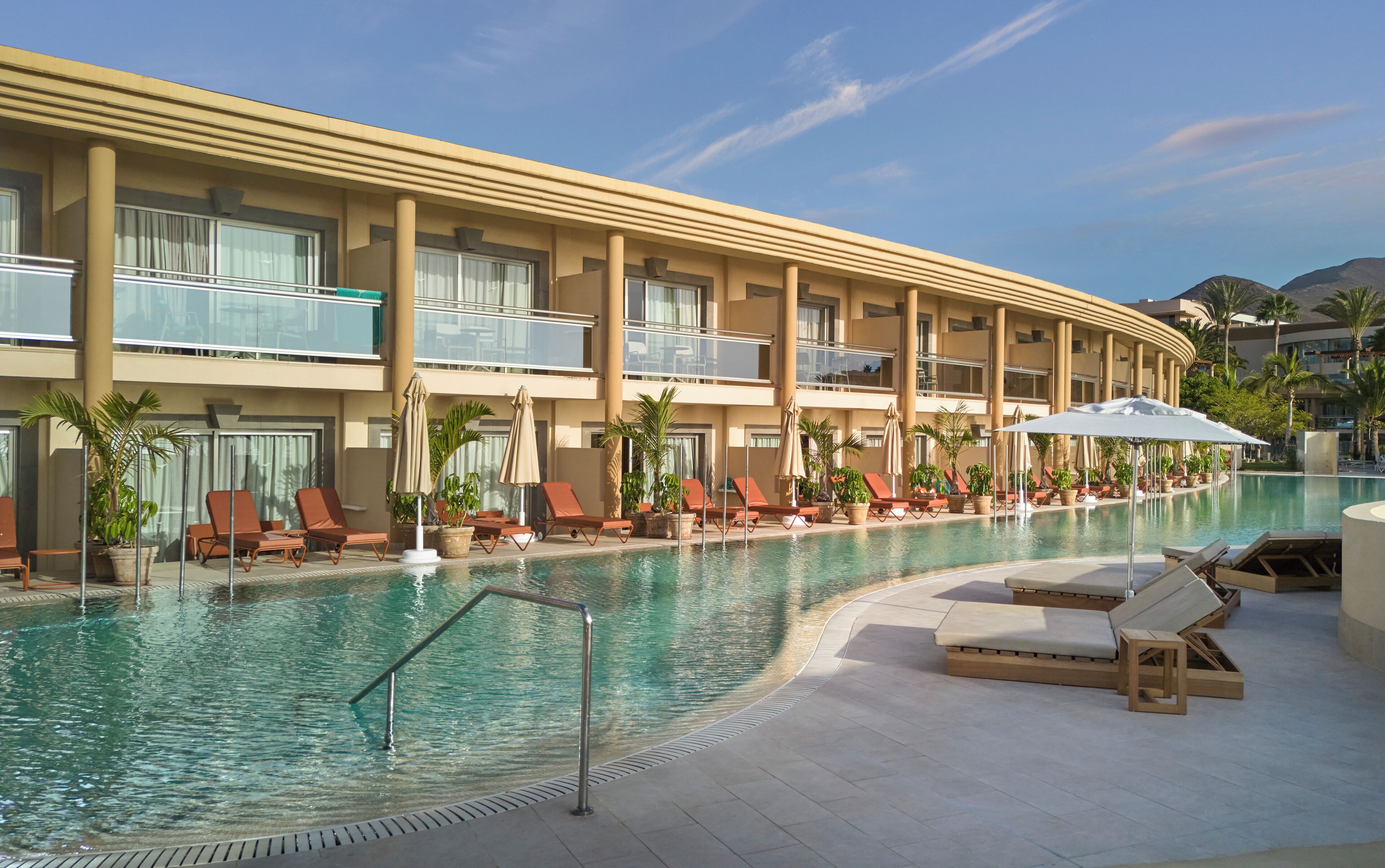 Un hôtel doté d’une piscine, de chaises longues et de plantes en pot.