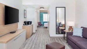 A modern hotel room with a flat-screen TV, a sofa, a coffee table, a desk with a computer, and a mirror. - Hilton Garden Inn Miami Airport West (Miami)