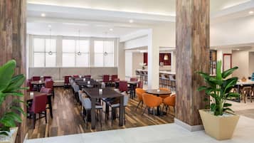 A spacious dining area with multiple tables and chairs, large windows, and a wooden column.