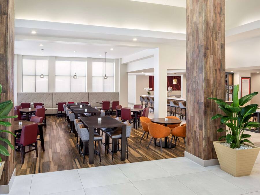 A spacious dining area with multiple tables and chairs, large windows, and a wooden column.
