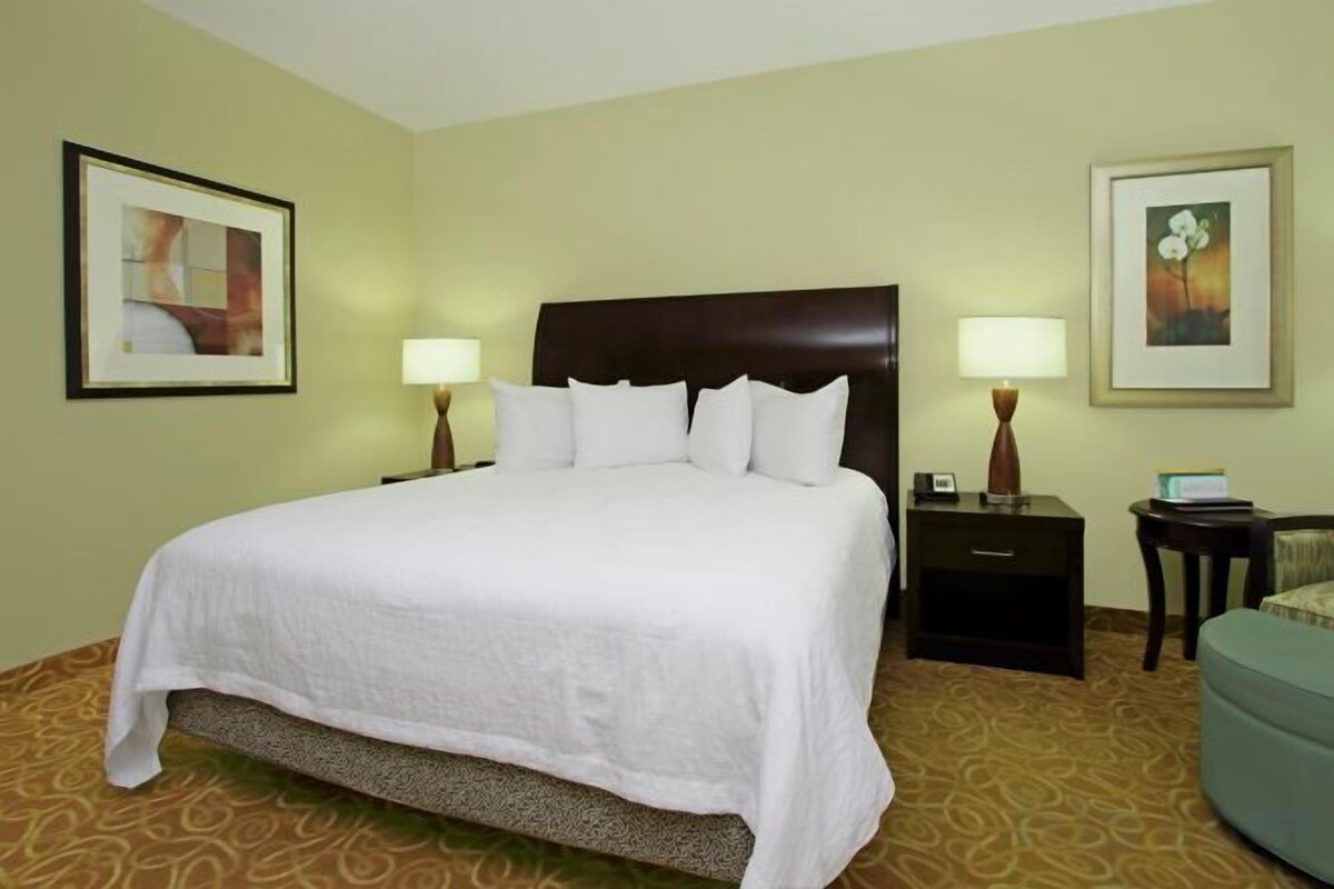 A hotel room with a large bed, two bedside tables with lamps, a chair, and artwork on the walls.