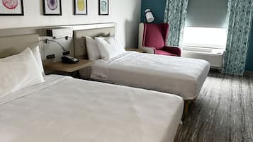 A hotel room with two beds, a desk, a chair, a lamp, and a window with curtains.
