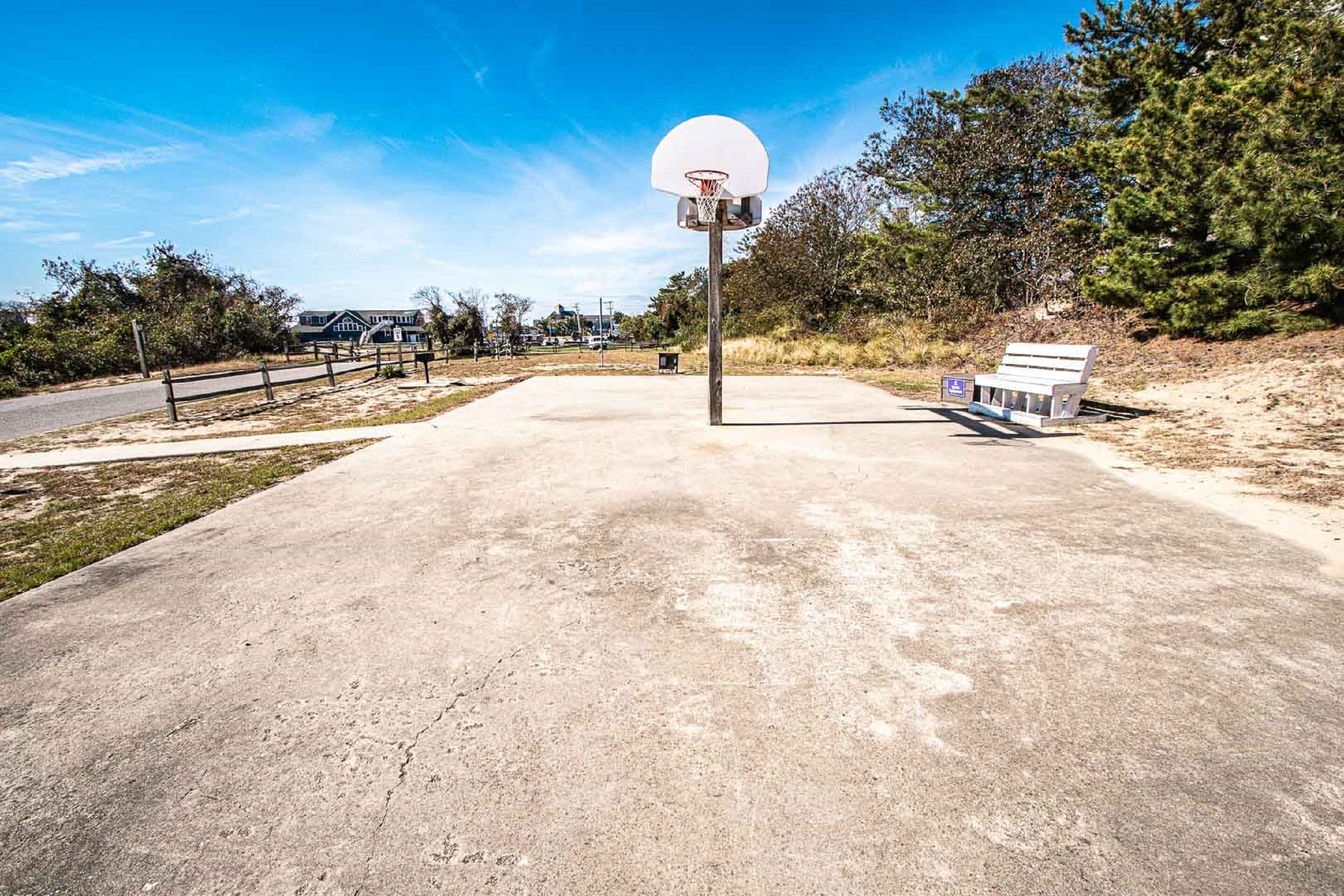 An outdoor basketball court with a hoop, a bench, and a paved area.