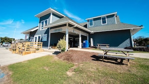 A two-story building with a covered entrance, outdoor seating, and a sign for a coffee shop. - Barrier Island Station (Kitty Hawk)