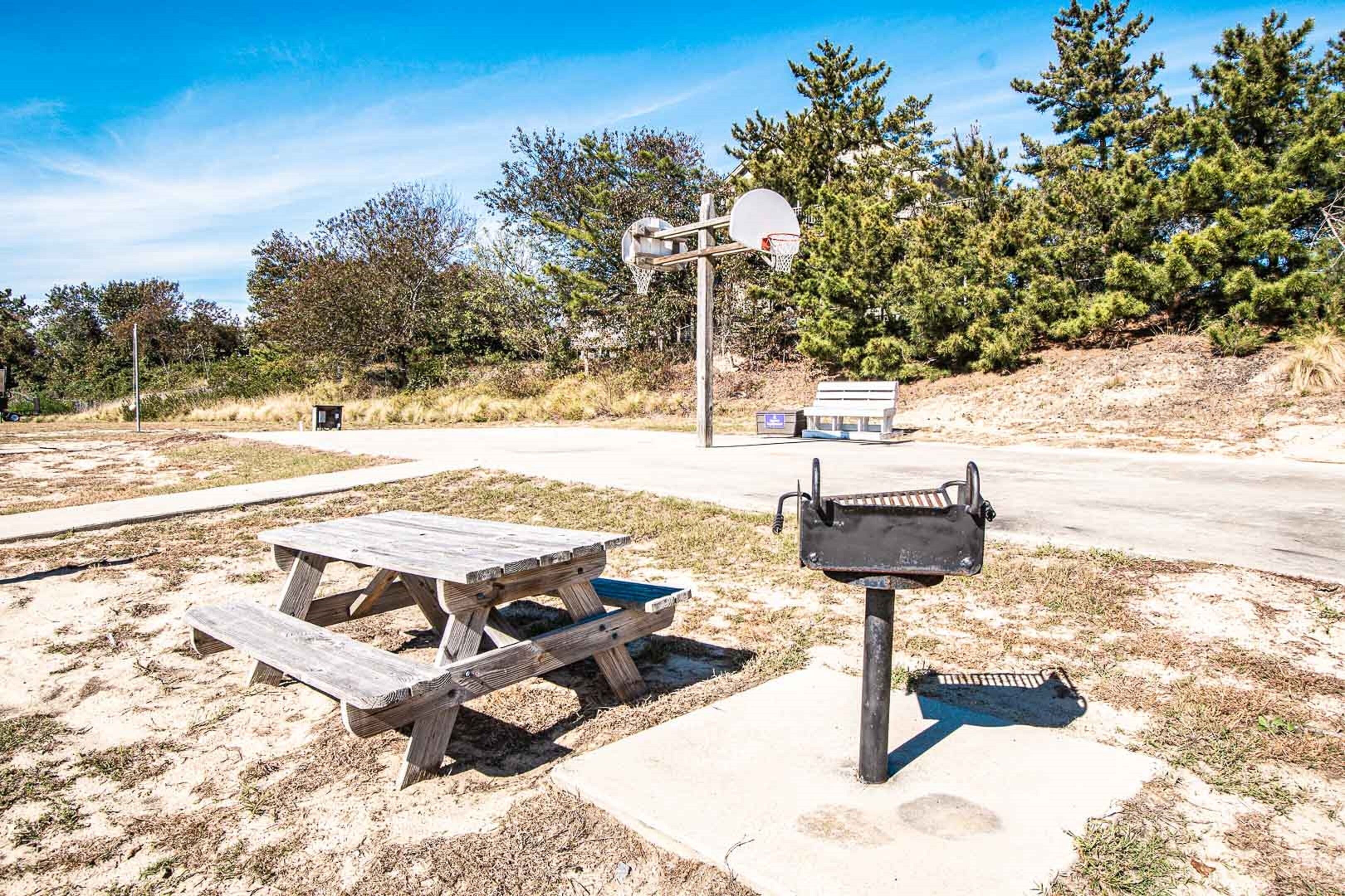 A picnic table, a barbecue grill, and a basketball hoop in an outdoor setting.
