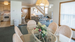 A spacious living area with a dining table surrounded by wicker chairs, a sofa, and a staircase leading to another level. - Barrier Island Station (Kitty Hawk)