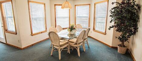 A dining area with a glass table surrounded by wicker chairs, a hanging light fixture, and a potted plant.