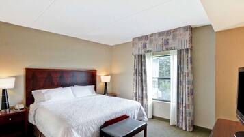 Hotelkamer met een groot bed, een houten hoofdbord, een nachtkastje met een lamp, een bankje, een televisie en een raam met gordijnen.