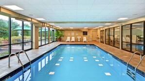 An indoor swimming pool with clear glass walls, a tiled floor, and a ceiling with recessed lighting.