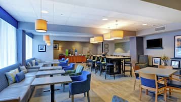 Una moderna hall d'albergo con zone salotto, un bar e uno schermo televisivo.