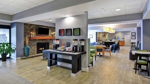 A modern hotel lobby with a fireplace, a coffee bar, and seating areas.