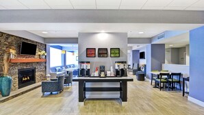 A modern lobby with a fireplace, seating area, coffee station, and a dining area.