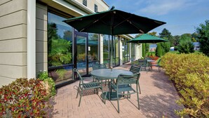 An outdoor patio with a round table and chairs, two green umbrellas, and a brick floor.