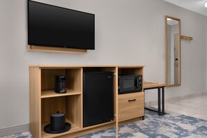 Een moderne kamer met een flatscreen televisie aan de muur, een ingebouwde magnetron, koffiezetapparaat en een koelkast in een houten kast.