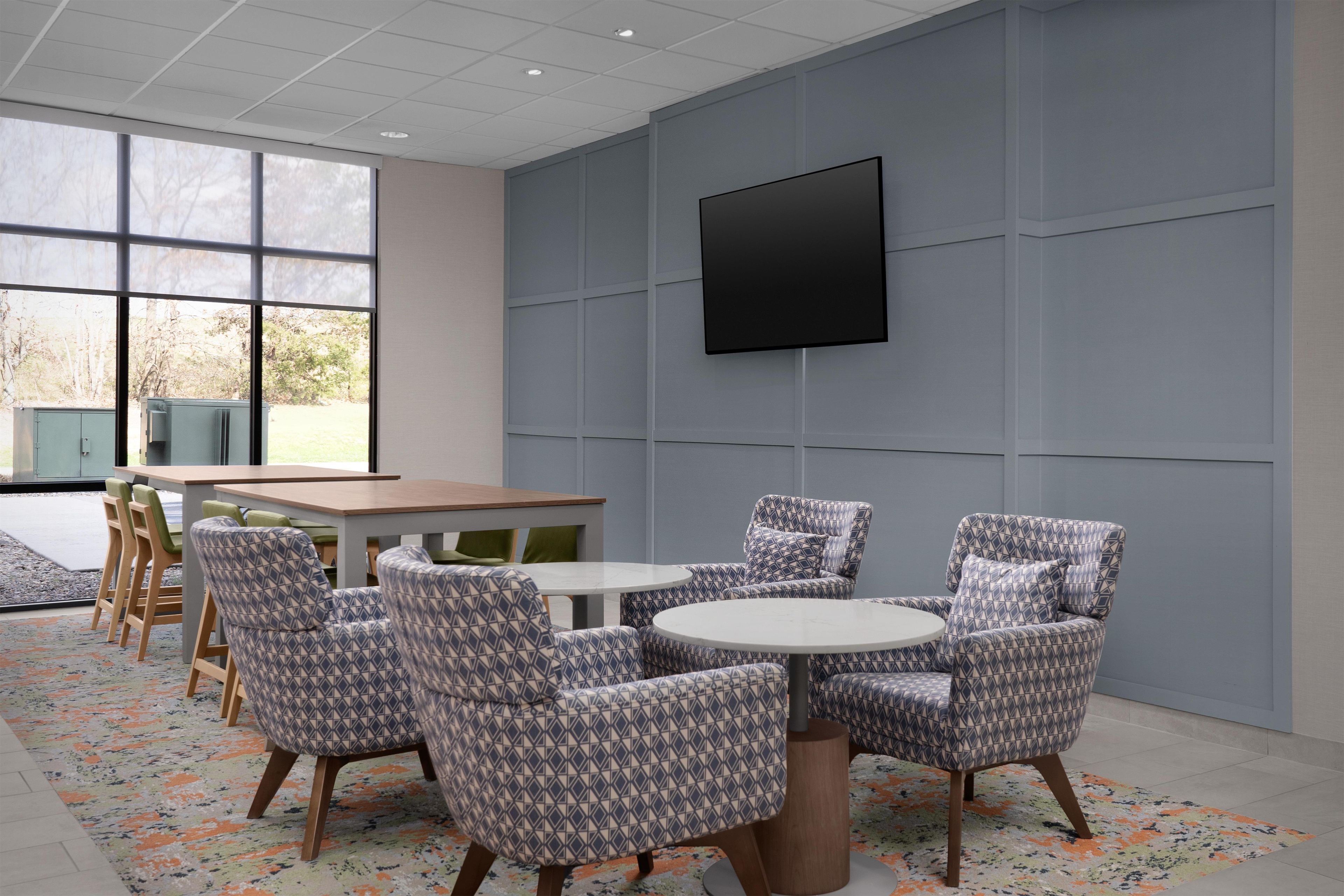 A modern meeting room with a large table, patterned chairs, a flat-screen TV, and large windows.