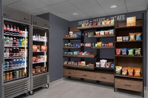 A snack and beverage display area with refrigerated drinks and shelves stocked with snacks and treats. - Hampton Inn Crossville (Crossville)