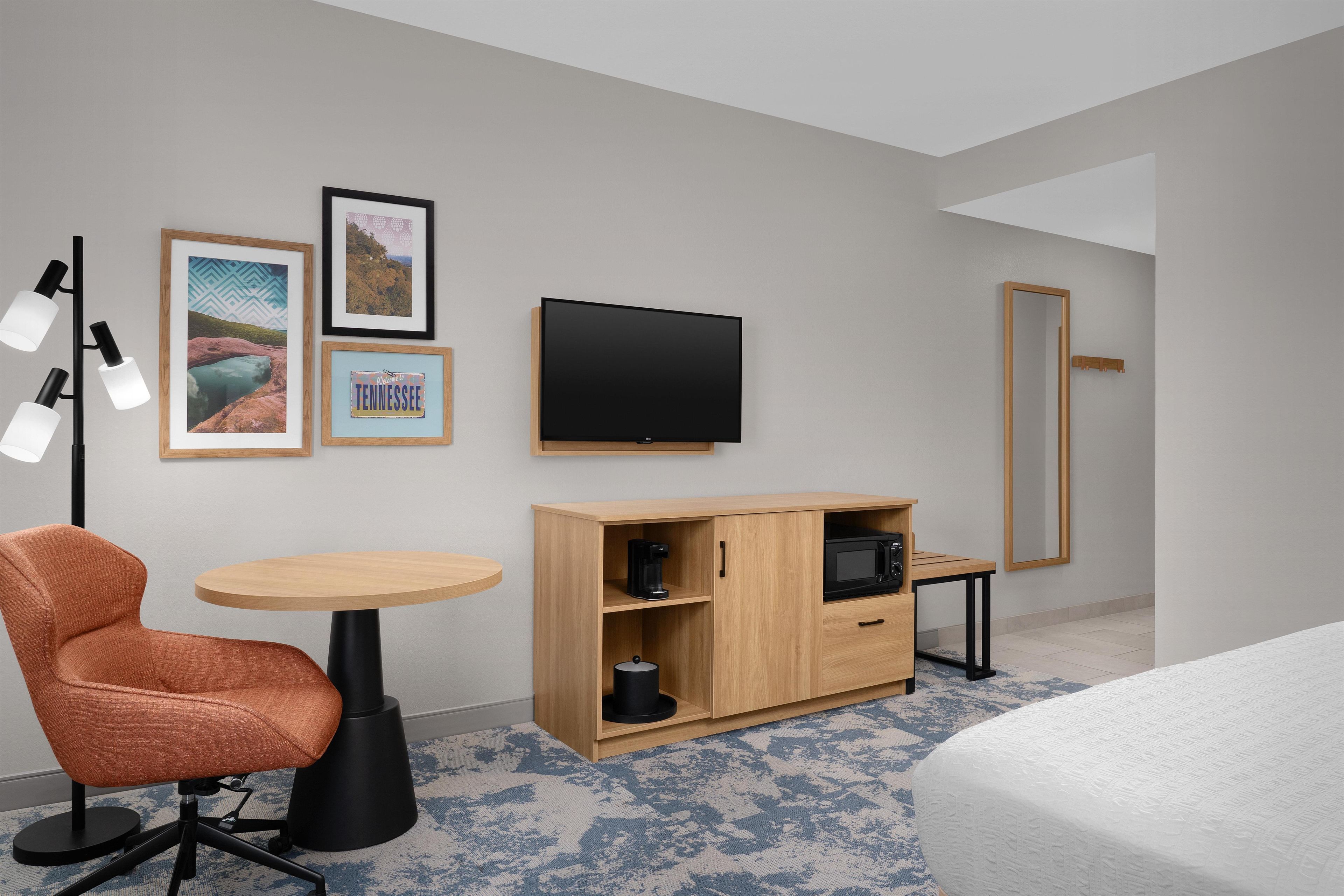 A hotel room with a bed, a desk, a chair, a wardrobe, a television, and framed pictures on the wall.