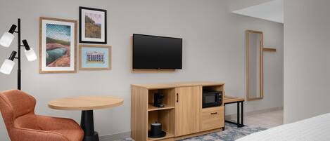 A hotel room with a bed, a desk, a chair, a wardrobe, a television, and framed pictures on the wall.