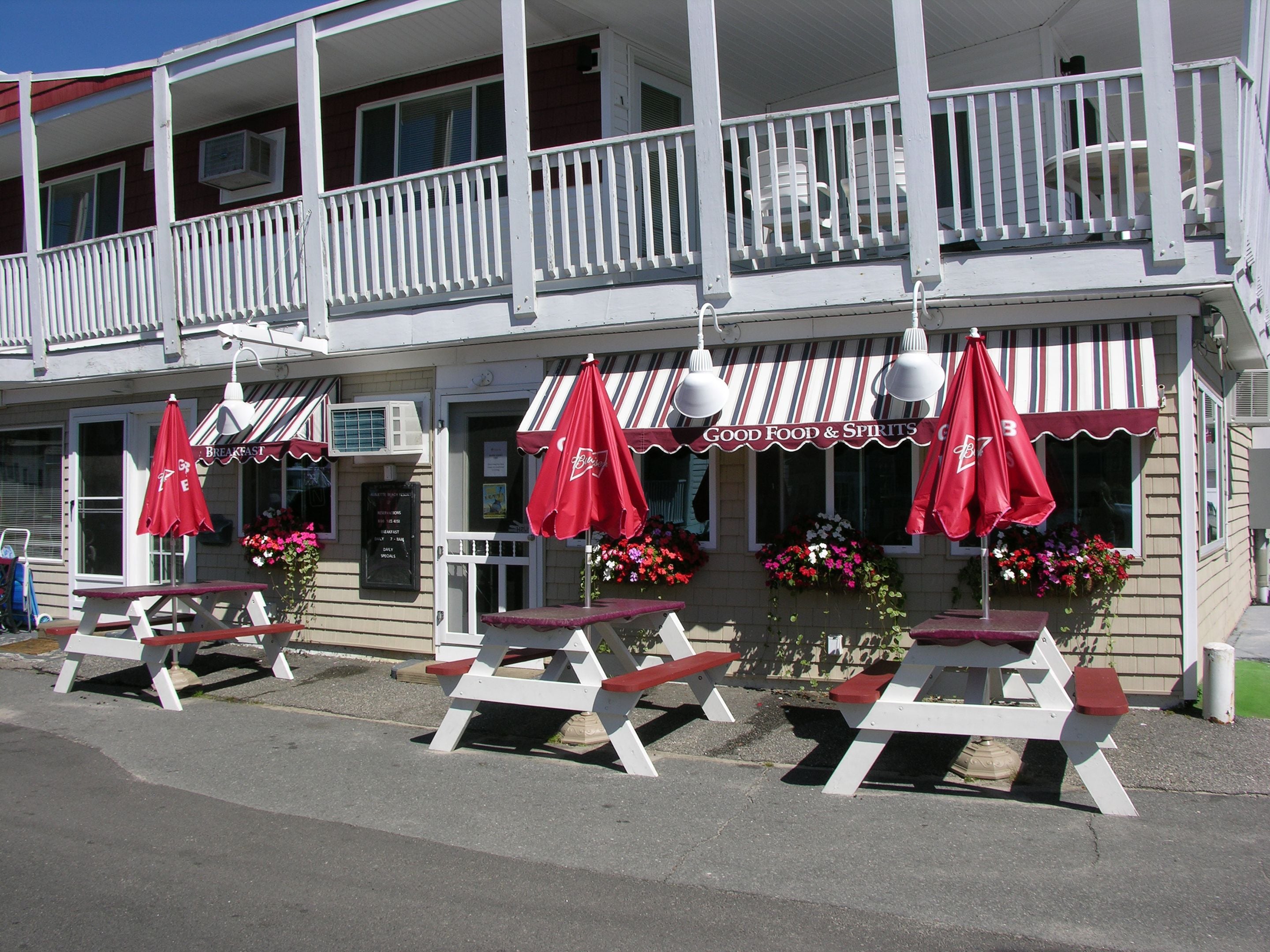 A restaurant with outdoor seating, red umbrellas, and a sign reading "Good Food & Spirits".