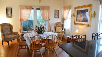 Un comedor con una mesa preparada para cuatro personas, rodeada de sillas de madera, un sillón estampado y un cuadro grande en la pared.