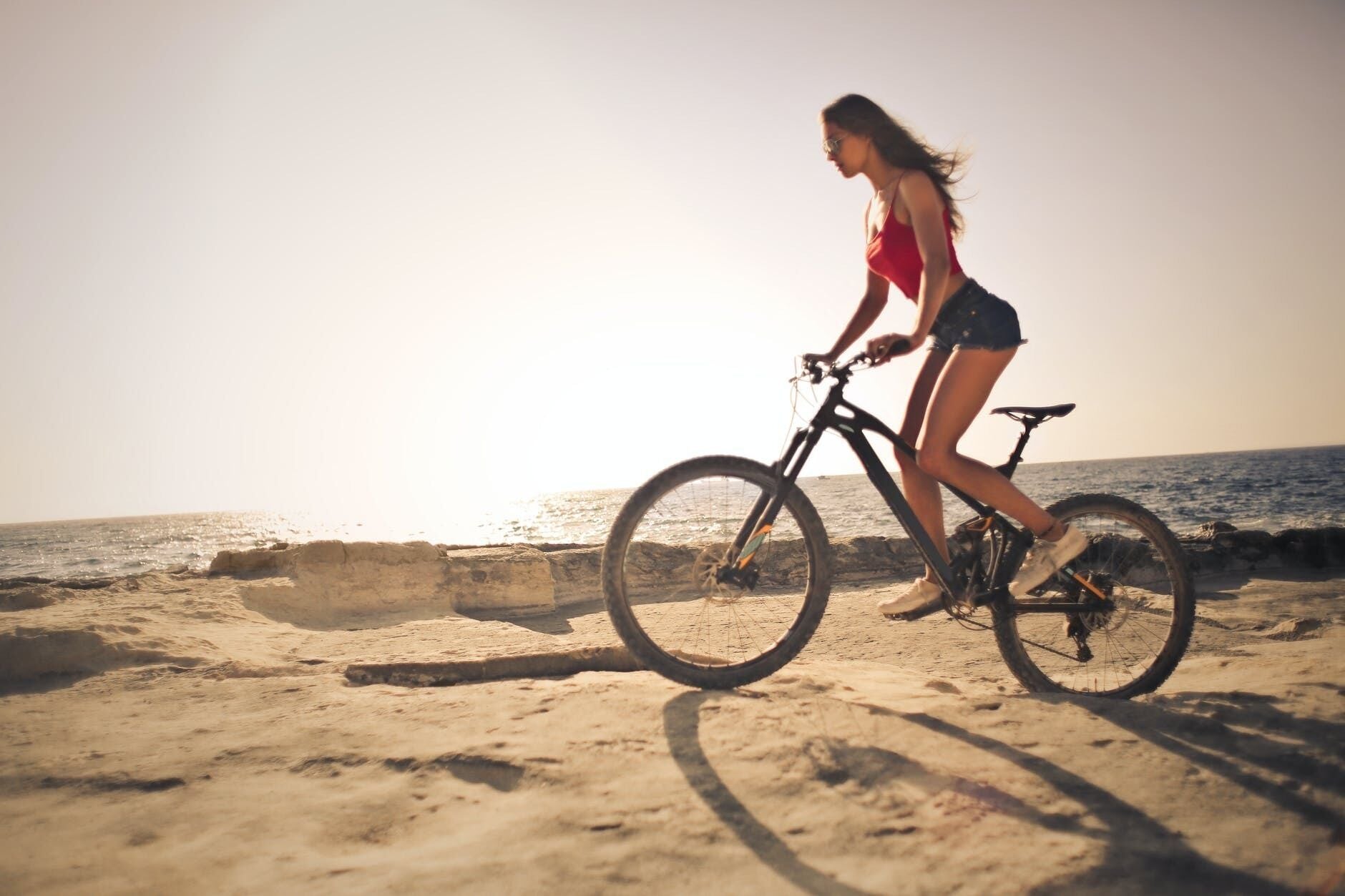 Une personne fait du vélo sur une plage de sable, avec l’océan en arrière-plan.