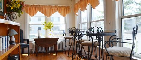 A cozy room with a wooden floor, a radiator, a table with chairs, and a bookshelf with books and a lamp.