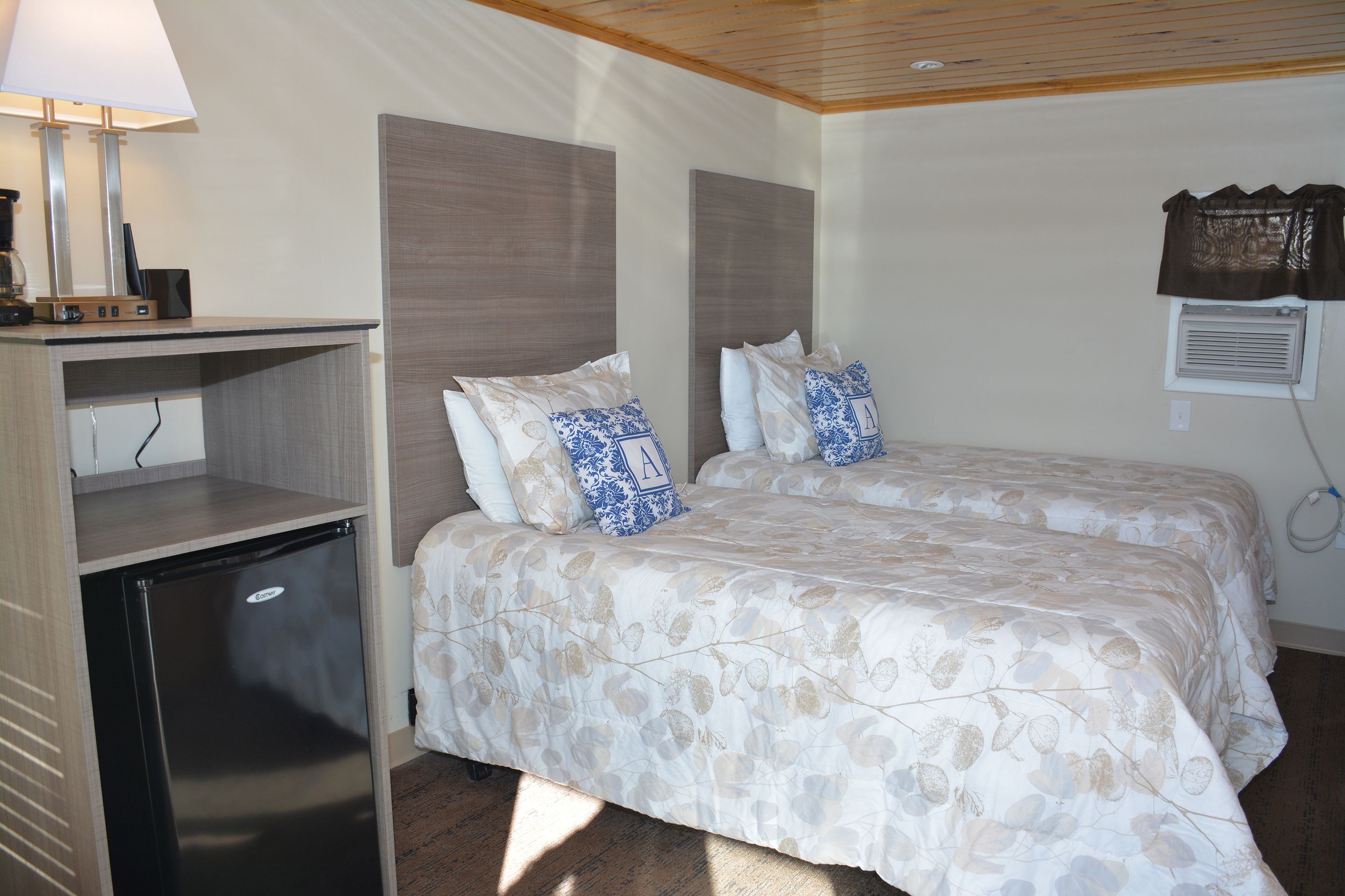 A bedroom with a bed, a desk with a lamp, and a small refrigerator.