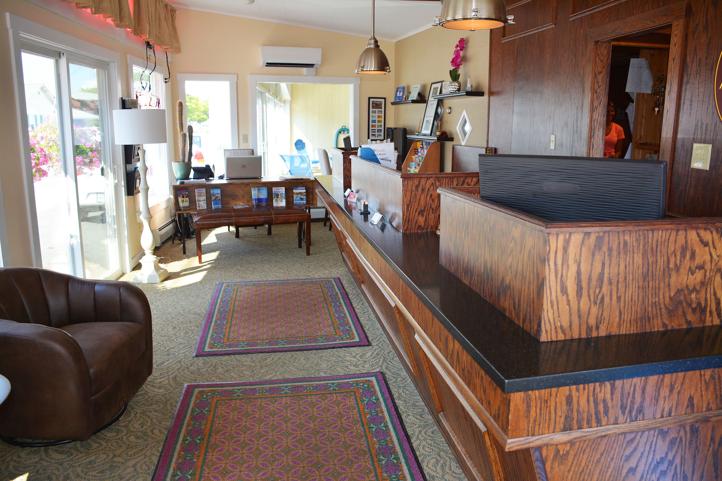 A reception area with a wooden reception desk, a brown leather sofa, and a large window with a view of the outside.