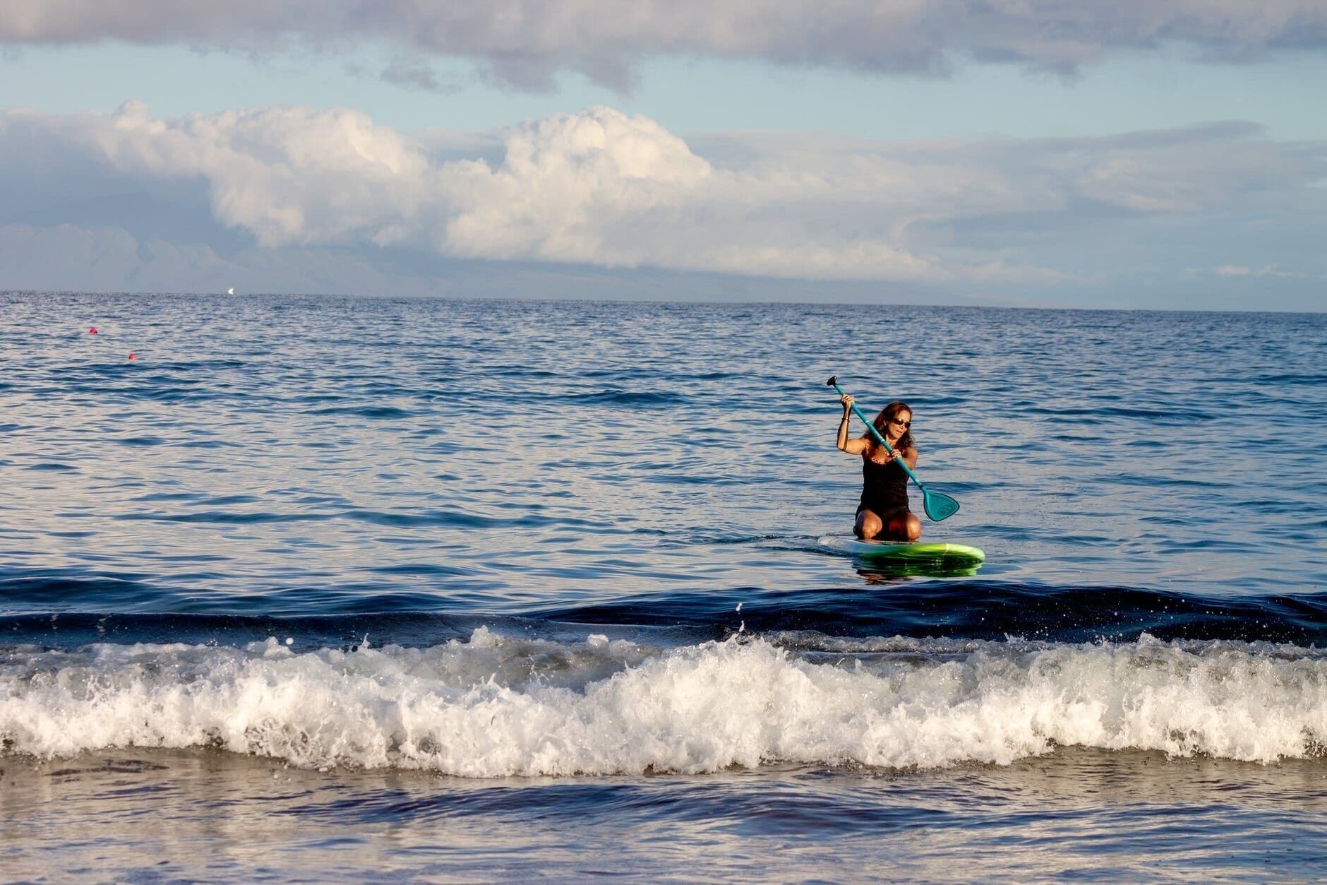 A person paddleboarding on a calm sea with waves breaking near the shore.