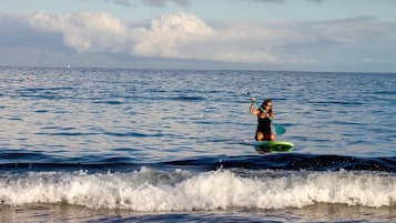 A person paddleboarding on a calm sea with waves breaking near the shore.