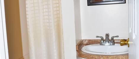 A bathroom with a shower curtain, a sink with a mirror above it, and a toilet.