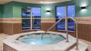 Un jacuzzi con escalera metálica, rodeado de paredes color turquesa y ventanas grandes.