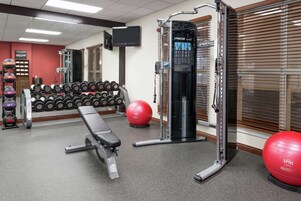 Un gimnasio con equipamiento de levantamiento de pesas, mancuernas y pelotas de ejercicio.